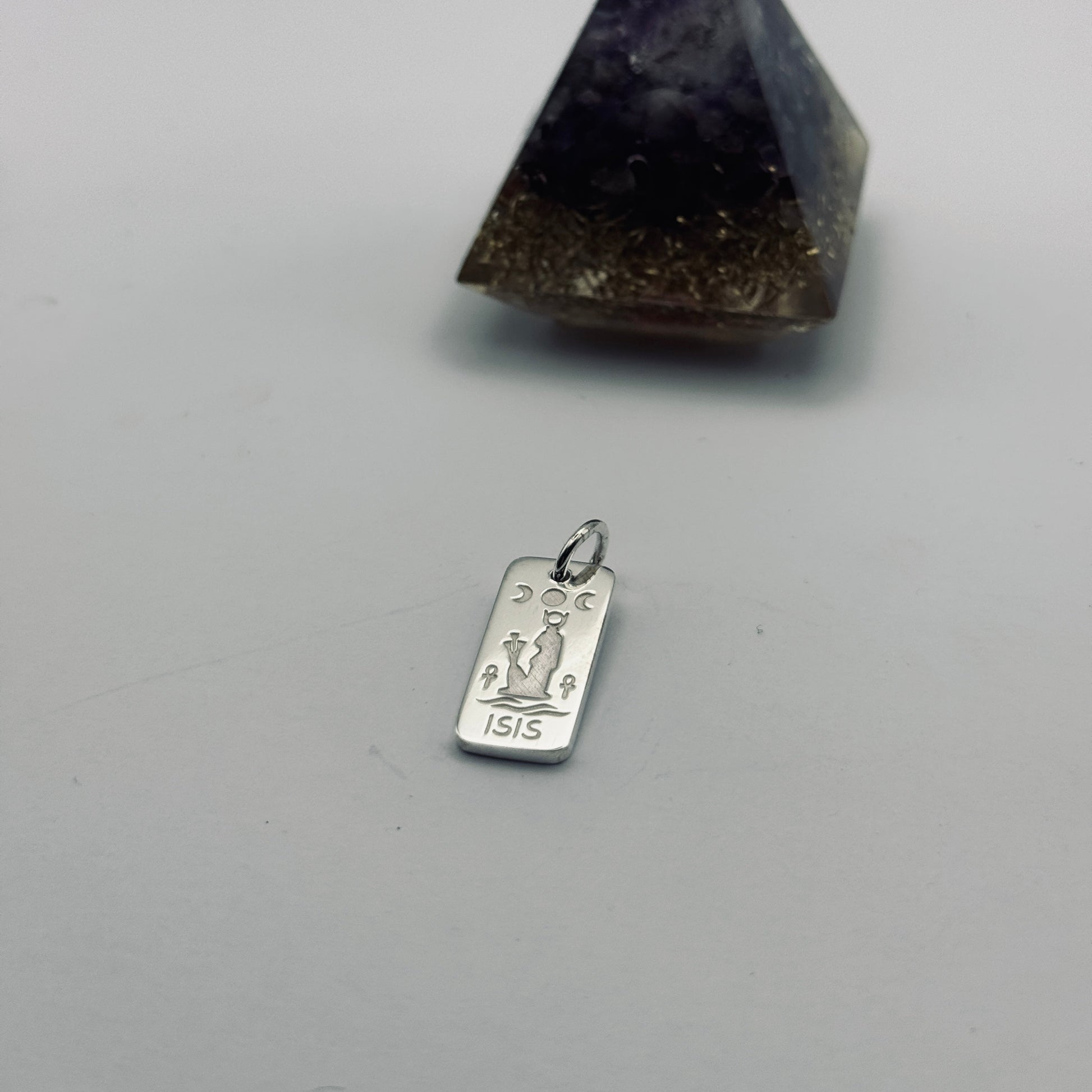A silver-toned metal pendant charm engraved with a tarot card and the year '1915', shown next to a dark purple and brown amethyst pyramid crystal on a light gray background.